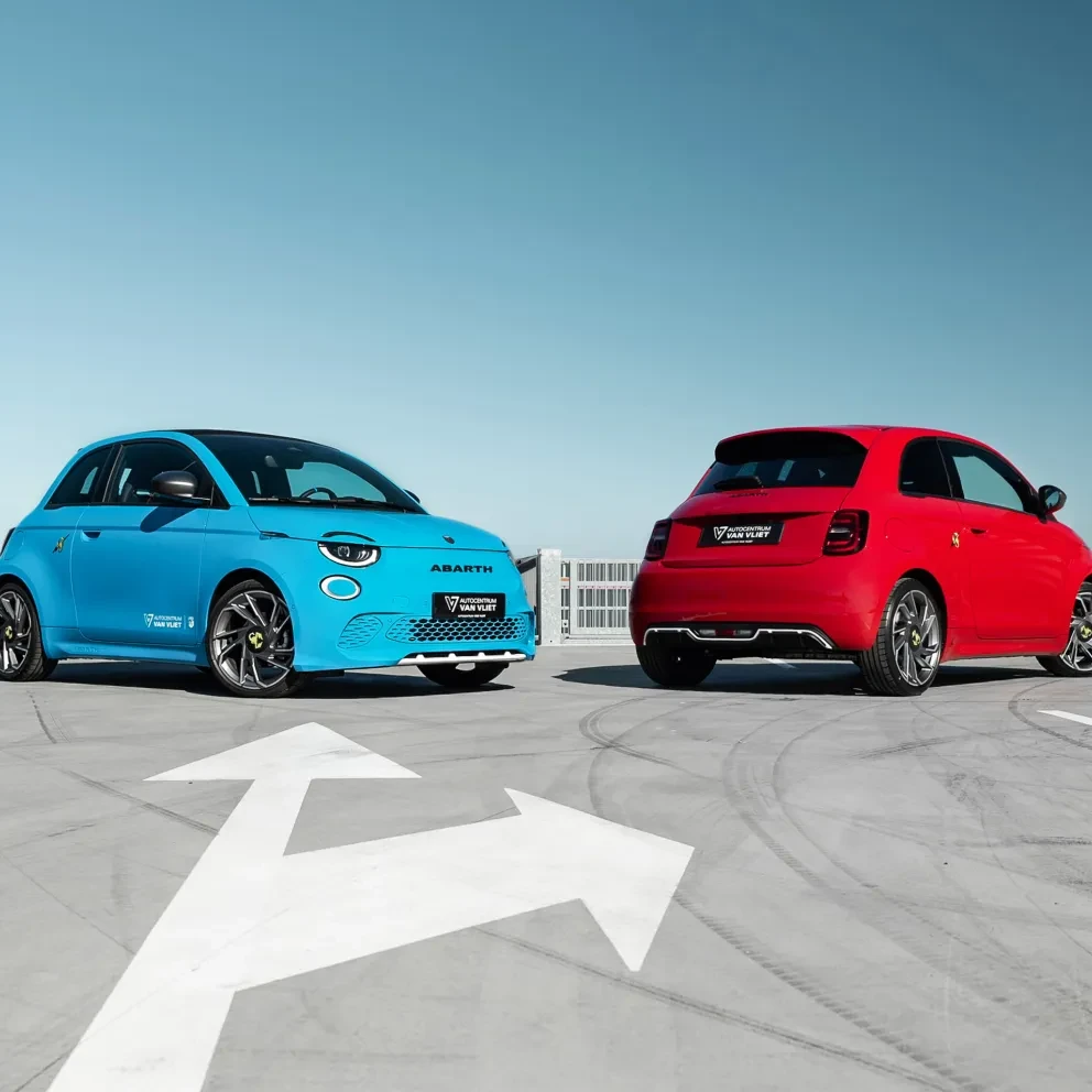 Twee Abarth 500's, één in felblauw en één in rood, staan sportief gepositioneerd op een leeg parkeerdek 