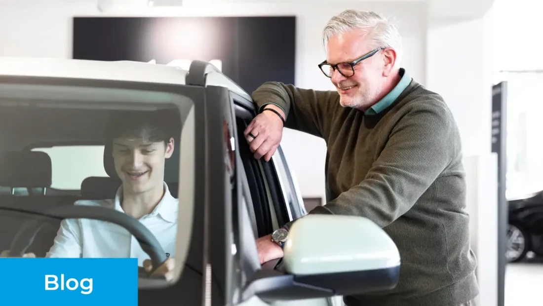 Verkoopadviseur staat buiten een Kia en vertelt over de functies van deze auto aan de klant op de bestuurdersstoel.